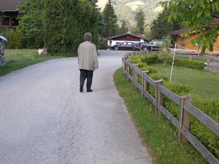 Ältere Frau geht auf Straße neben Zaun