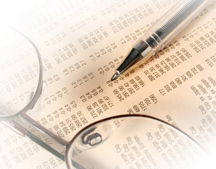 Pen and reading glasses rest on financial newspaper.