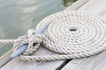 Coiled mooring line tied around cleat on a wooden dock