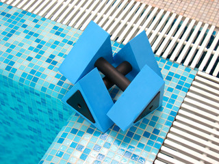 two blue aqua dumbbells lie on the coast swimming-pool