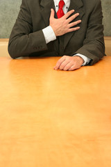 Business-man sitting at the desk, hands to his heart.