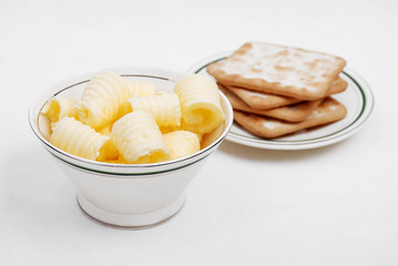 Butter curls in a bowl with crackers on white background