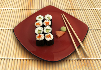 Sushi rolls on red plate with ginger and wasabi, on bambo mat.