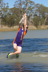 a teenage girl is swinging on a rope over a river in summer