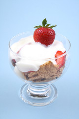 glass of yogurt fresh strawberries and cereals on blue