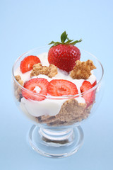 glass of yogurt fresh strawberries and cereals on blue