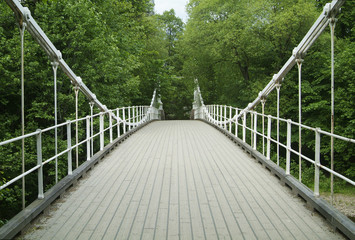 Old, white suspension bridge in a forest, made of wood and iron.