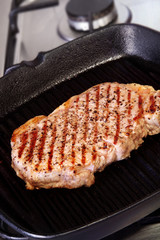 Beef steak cooking in a cast-iron grill pan.