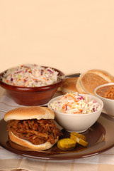 A pulled pork sandwich with cole slaw, baked beans and pickles