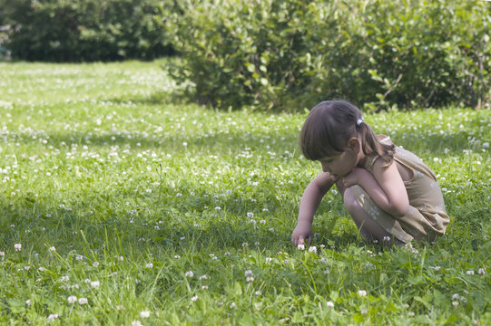 Little stylish girl is playing in the grass in clover meadow