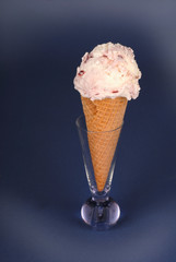 A scoop of cherry vanilla ice cream in a waffle cone