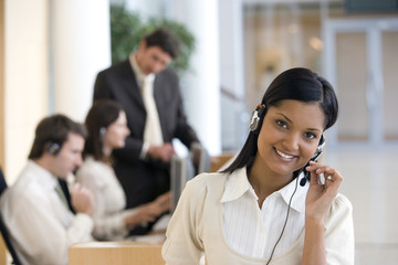 Business woman on headset with seated working colleagues hehind
