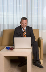 Businessman smiling working on his laptop sitting in sofa