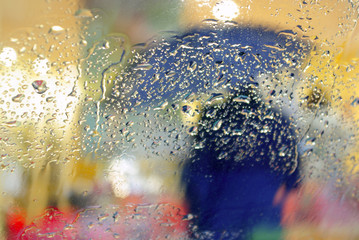 Silhouette of a person with umbrella through wet windshield.