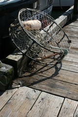 A cylindrical empty crab pot propped up on a wooden dock