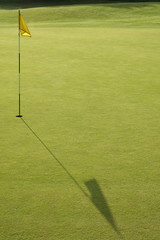 golf green and flag with long shadows
