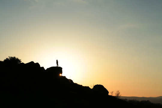 Girl silhouetted against the setting sun,stood on rock outcrop