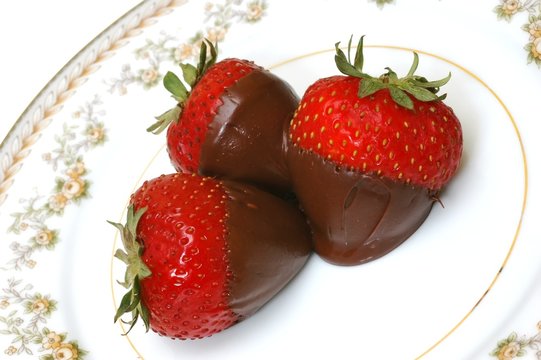 Three chocolate dipped strawberries on plate.