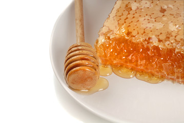 A honeycomb with a honey wand on a white plate overhead view