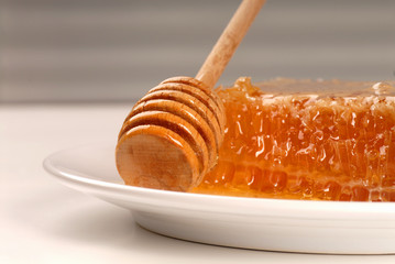 A honeycomb with a honey wand on a white plate