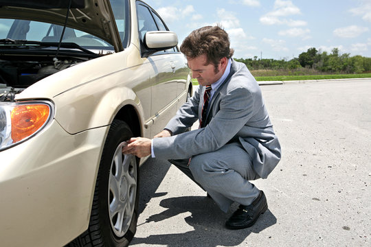 A businessman has a flat tire on the road.