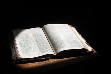 Old open bible lying on a wooden table in a beam of sunlight 