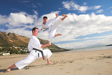 Young adult men with black belt practicing on the beach 