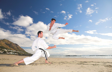 Young adult men with black belt practicing on the beach