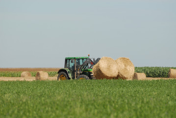 Tracteur rassemblant des bottes de paille en plaine