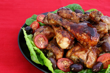 A platter of barbecued chicken drumsticks, on a red tablecloth.