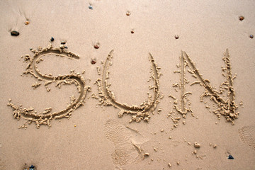 Fototapeta na wymiar Słowo Sun napisana w piasku obok brzegu