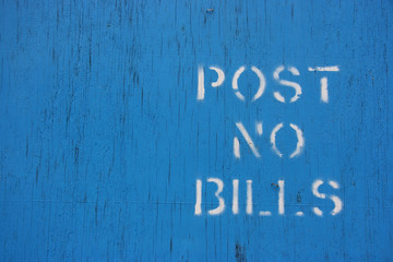 Blue wooden panel with a white stenciled "post no bills" text