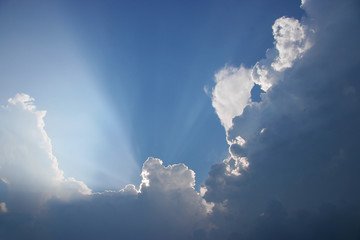 Sun projecting rays behind clouds in the blue sky 