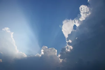 Papier Peint photo Lavable Ciel Sun projecting rays behind clouds in the blue sky 
