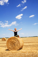 Naklejka na ściany i meble Woman enjoying the summer sun sitting on a hay bale