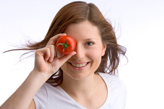 junges, schönes Mädchen hält eine Tomate zu ihrem Auge