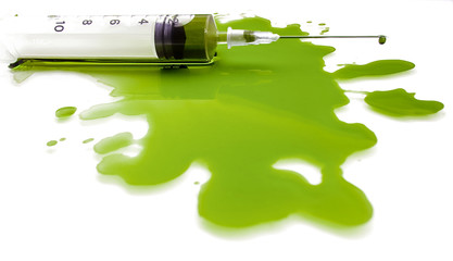 Syringe in a pool of a green liquid on a white background