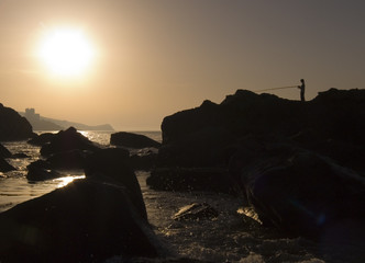 Silhouette of the fisherman with a fishing tackle on dawn