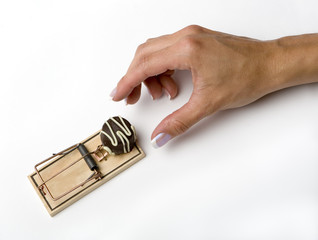 a woman's hand reaching for a chocolate in a mousetrap