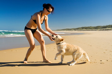 Bikini girl playing with puppy on the beach