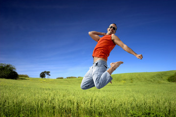 Man jumping on a green meadow with a beautiful cloudy sky