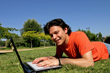 young man lying in the grass and working with laptop