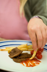 Child eating steak and chips with sauce