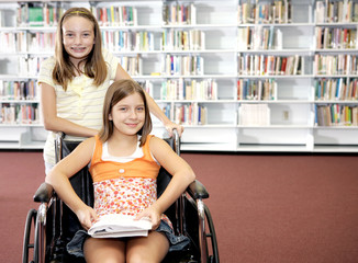 Two school girls at the library.  One is in a wheelchair.