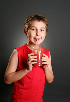 A young boy holds a fresh berry juice in a clear container