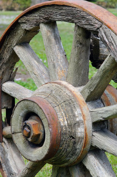 Old, wooden, rustic wagon wheel in a grassy field.