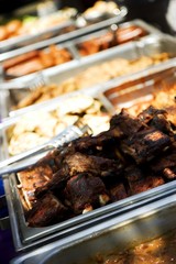 Trays of juicy barbecue food, focus on ribs in front