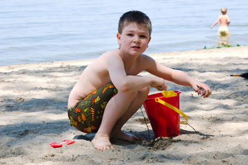 A young boy plays in the sand with his bucket and shovel