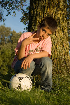 boy shows the peacesign and holds a soccerball