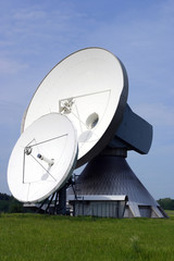 Two satellite dishes with blue sky and green grass.